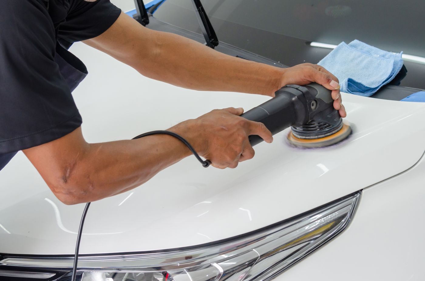 A detailer using an orbital polisher on a car hood, for illustration
