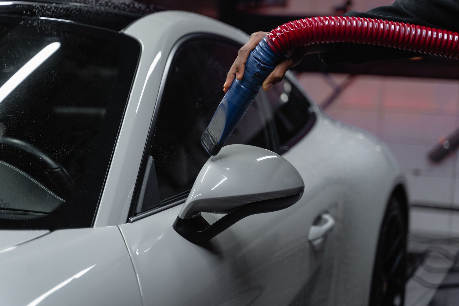 A detailer cleaning a car's side mirror with a detail brush, for illustration